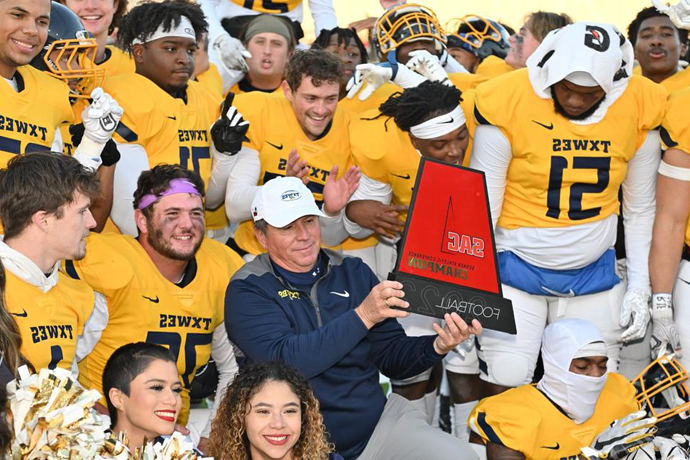 Head football coach joe prud'homme and the texas wesleyan football team pose with the 2022 sooner athletic conference champions trophy