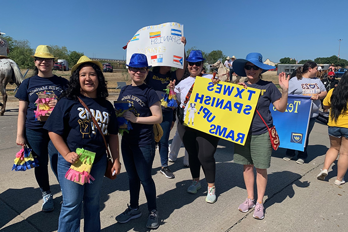 A group of Texas Wesleyan students in hats gold a yellow sign that says TXWES Spanish